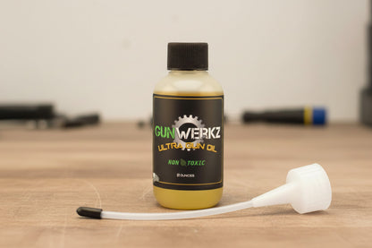 Bottle of 2 ounce ultra gun lube with extend-a-spout in front of bottle on a butcher block top with a blurred  background